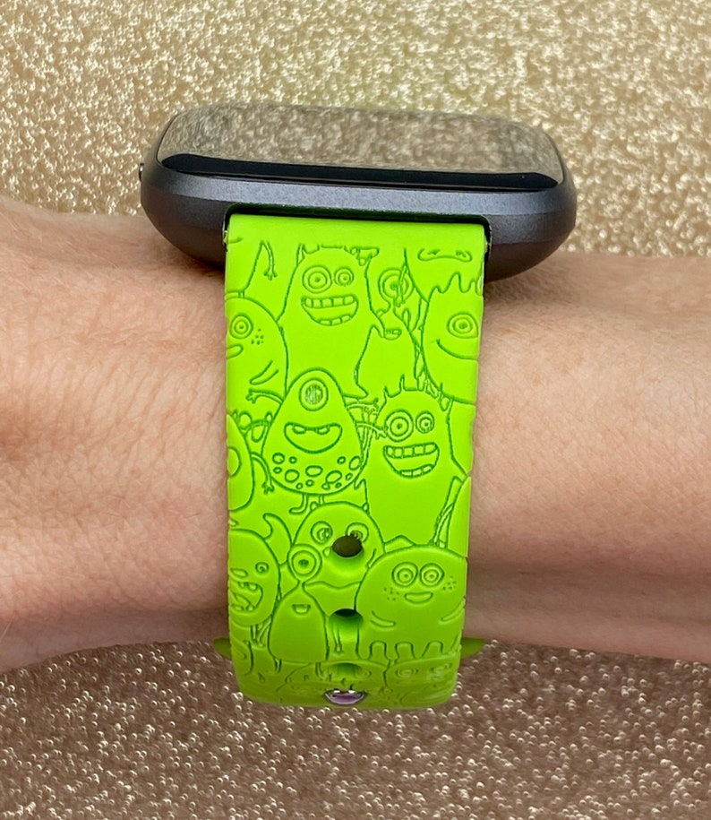 Puede incluir: Una correa de reloj de silicona verde con un estampado de monstruo de dibujos animados. La correa est&aacute; dise&ntilde;ada para un reloj inteligente con una esfera negra.