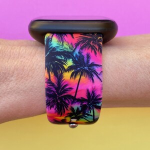 May include: A black smartwatch with a vibrant watch band featuring a tropical palm tree design. The band showcases a colorful gradient of pink, yellow, and blue hues, creating a summery aesthetic. The band is attached to the watch with a silver pin.