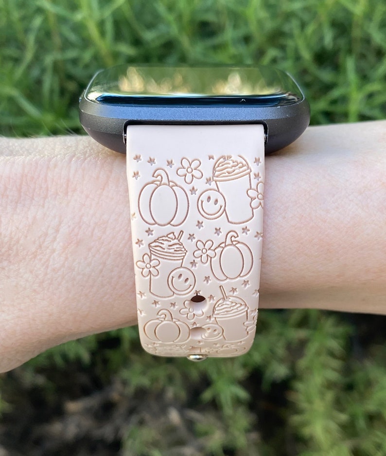 May include: A light pink silicone watch band with a fall-themed design. The band features pumpkins, coffee cups, and stars.