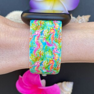Puede incluir: Una correa de reloj azul turquesa y rosa con un patr&oacute;n de caballitos de mar. La correa est&aacute; hecha de silicona y es compatible con Apple Watch.