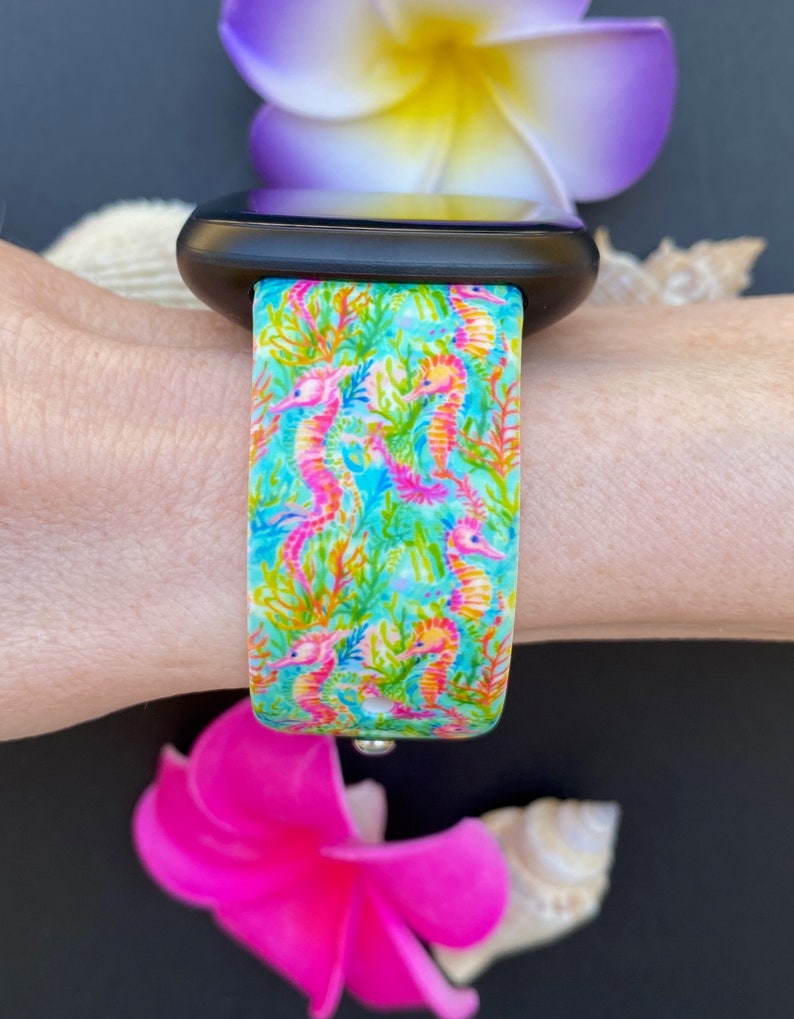 Puede incluir: Una correa de reloj azul turquesa y rosa con un patr&oacute;n de caballitos de mar. La correa est&aacute; hecha de silicona y es compatible con Apple Watch.