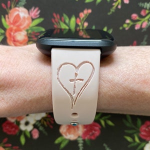 K&ouml;nnte beinhalten: Ein rosafarbenes Silikon-Armband mit einem Herz- und Kreuzdesign.