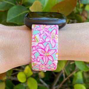 Puede incluir: Un reloj inteligente negro con una banda de patr&oacute;n floral. La banda es azul claro con flores rosas.