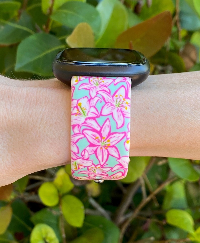 Puede incluir: Un reloj inteligente negro con una banda de patr&oacute;n floral. La banda es azul claro con flores rosas.