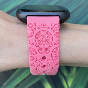 K&ouml;nnte beinhalten: Ein pinkfarbenes Silikon-Armband mit Totenkopf-Motiv. Das Armband ist kompatibel mit Fitbit-Uhren.