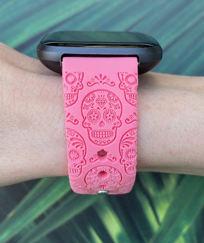 K&ouml;nnte beinhalten: Ein pinkfarbenes Silikon-Armband mit Totenkopf-Motiv. Das Armband ist kompatibel mit Fitbit-Uhren.