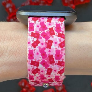 May include: A pink and red silicone watch band with a pattern of gummy bears and hearts. The band is on a black smartwatch.