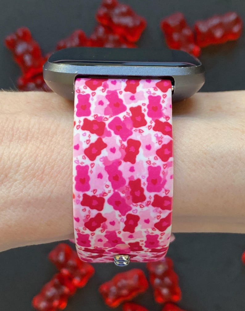 May include: A pink and red silicone watch band with a pattern of gummy bears and hearts. The band is on a black smartwatch.