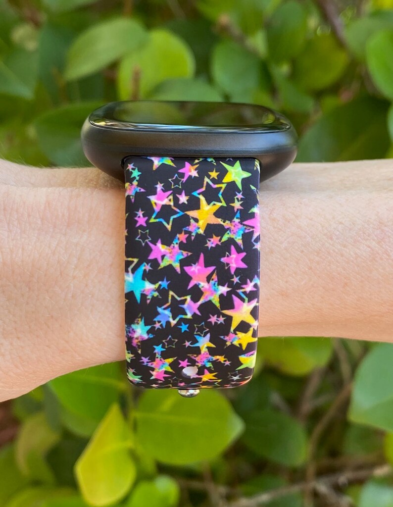 May include: A black fitness tracker with a colorful star pattern band. The band has pink, yellow, blue, and green stars on a black background.