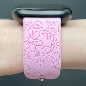 Puede incluir: Una correa de reloj de silicona rosa con un dise&ntilde;o floral y de caracol. La correa est&aacute; en la mu&ntilde;eca de una persona.