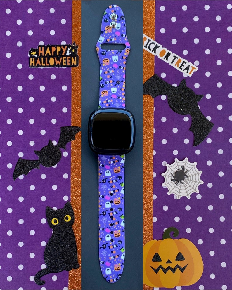 Puede incluir: Una banda de Apple Watch con estampado morado y negro con una esfera de reloj negra. La banda presenta una variedad de im&aacute;genes con tem&aacute;tica de Halloween, incluidos fantasmas, calabazas, murci&eacute;lagos y ma&iacute;z dulce. El reloj est&aacute; rodeado de decoraciones de Halloween, que incluyen un gato negro, una telara&ntilde;a y una calabaza.