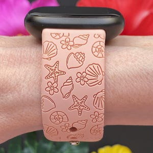 May include: A pink silicone watch band with a seashell and starfish pattern. The band is designed for a smartwatch.