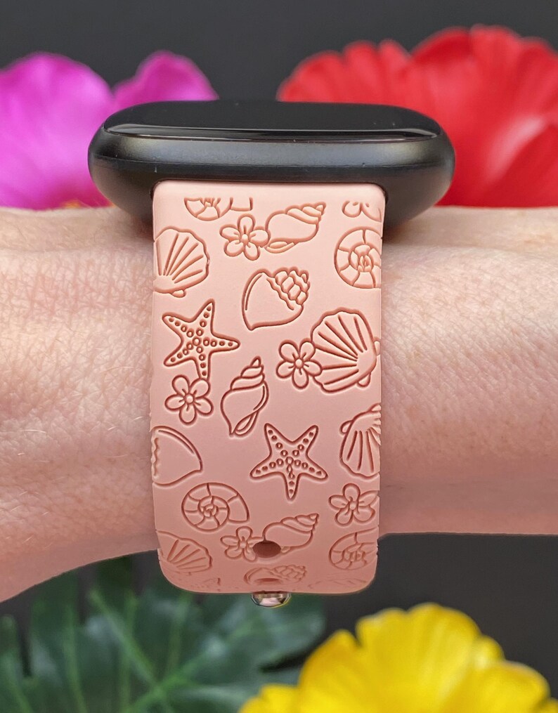 May include: A pink silicone watch band with a seashell and starfish pattern. The band is designed for a smartwatch.