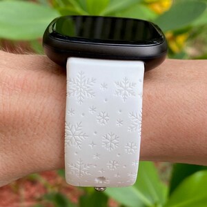Pu&ograve; includere: Smartwatch bianca con quadrante nero e cinturino bianco con motivo a fiocco di neve.