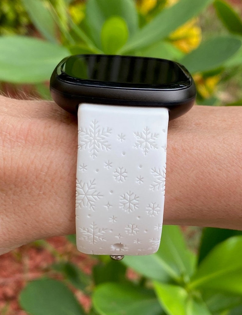 Pu&ograve; includere: Smartwatch bianca con quadrante nero e cinturino bianco con motivo a fiocco di neve.
