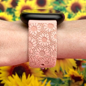 May include: A pink silicone watch band with a floral pattern. The band is designed to fit a smartwatch and has a textured surface.