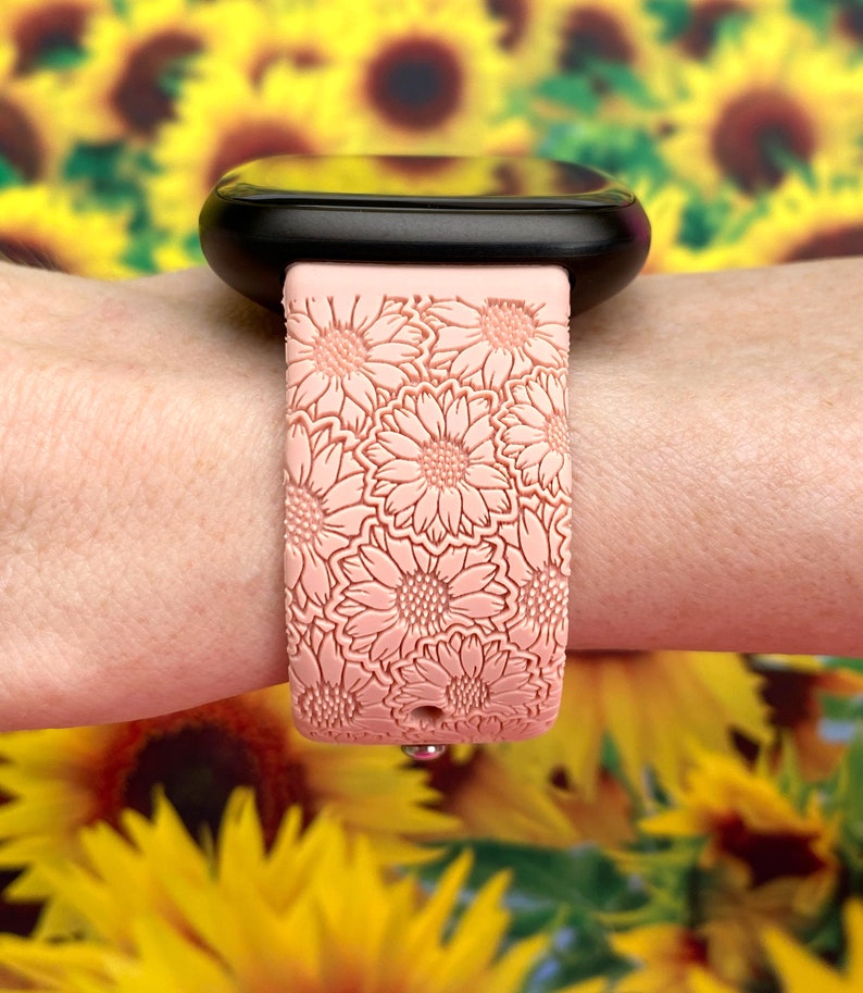 May include: A pink silicone watch band with a floral pattern. The band is designed to fit a smartwatch and has a textured surface.