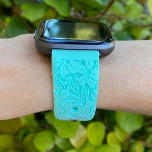 May include: A turquoise blue silicone watch strap with a floral pattern. The strap is designed for a smartwatch with a black screen.
