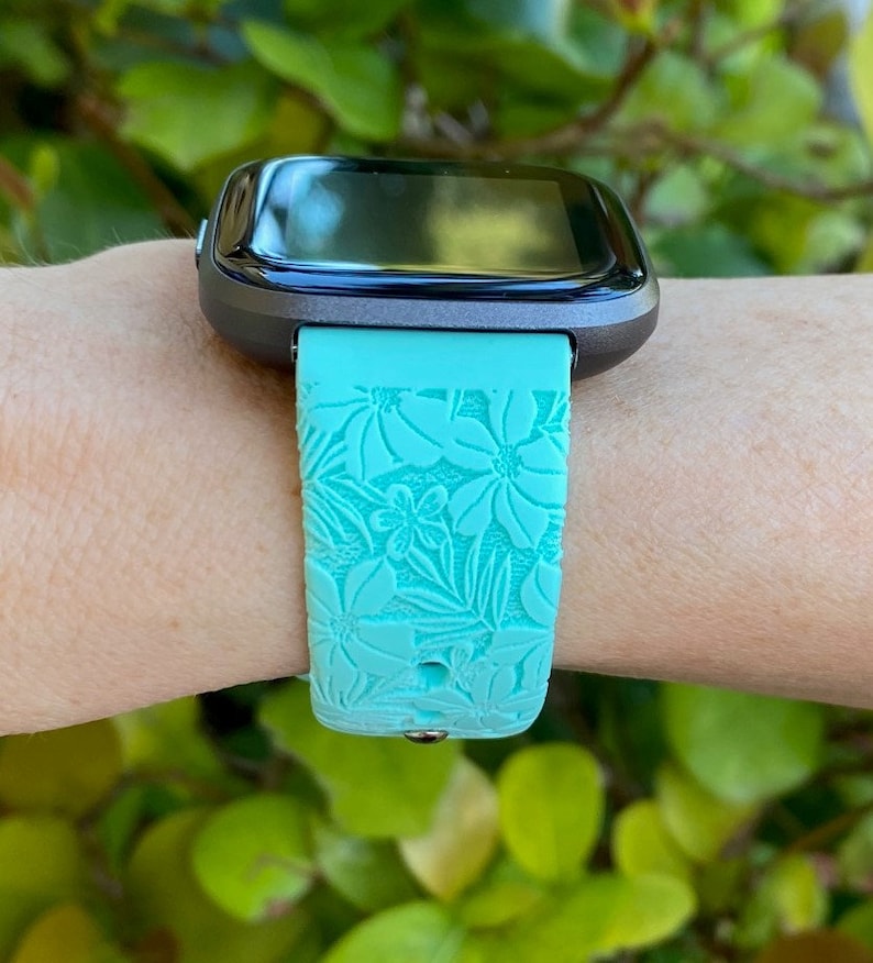 May include: A turquoise blue silicone watch strap with a floral pattern. The strap is designed for a smartwatch with a black screen.