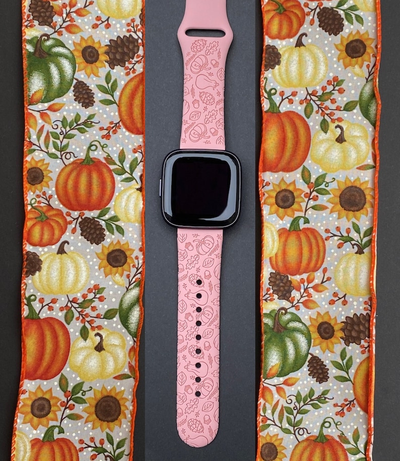 May include: A pink watch band with a fall-themed design featuring pumpkins, leaves, and acorns. The band is made of silicone and has a black watch face.