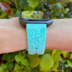 May include: A turquoise blue smartwatch band with a seashell and starfish design. The band is made of silicone and has a black watch face.