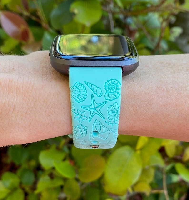 May include: A turquoise blue smartwatch band with a seashell and starfish design. The band is made of silicone and has a black watch face.
