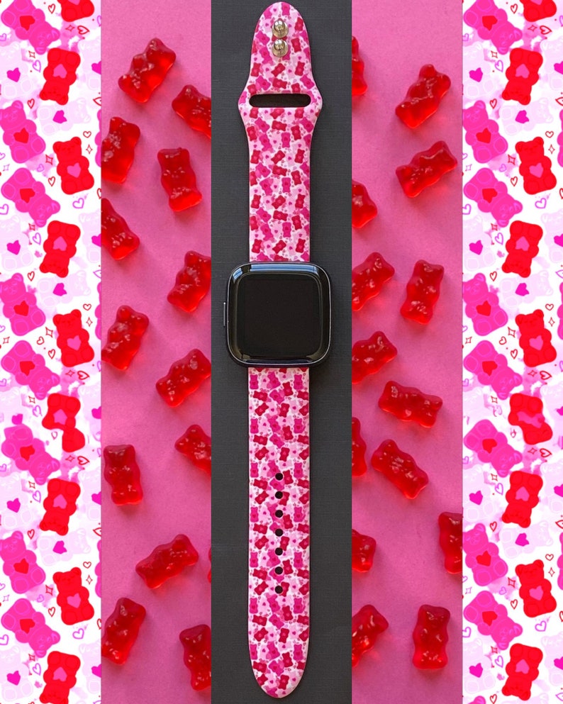 May include: A pink and white Apple Watch band with a gummy bear pattern. The band is made of silicone and has a black watch face.