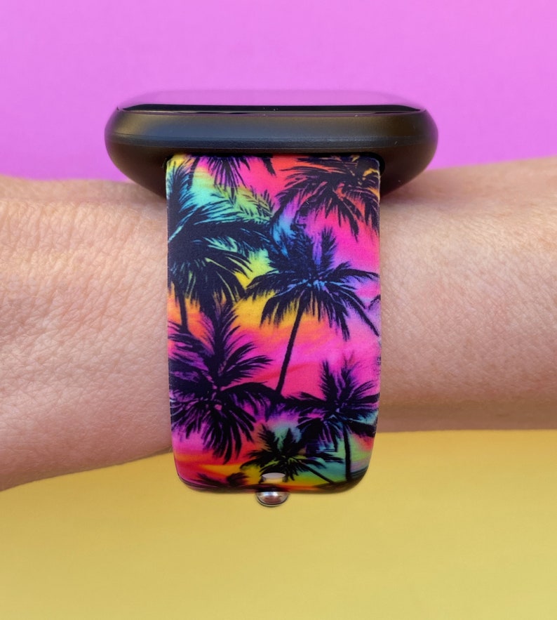 May include: A black smartwatch with a colorful palm tree print band. The band has a rainbow gradient background with black palm trees.
