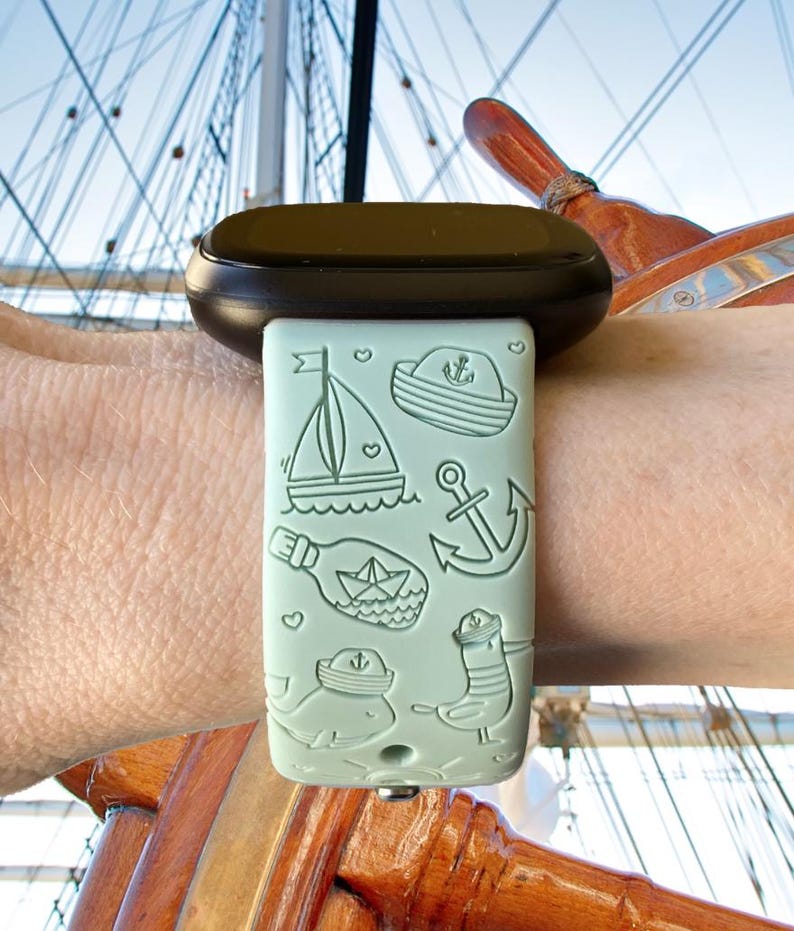 May include: A light green silicone watch band with a nautical theme. The band features a sailboat, anchor, bottle with a paper boat inside, whale, and a bird wearing a sailor hat.
