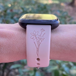Op de afbeelding: Een zwarte smartwatch met een roze siliconen band met een bloemenpatroon. De band heeft een delicaat bloemenpatroon dat in het siliconen is ge&euml;tst.