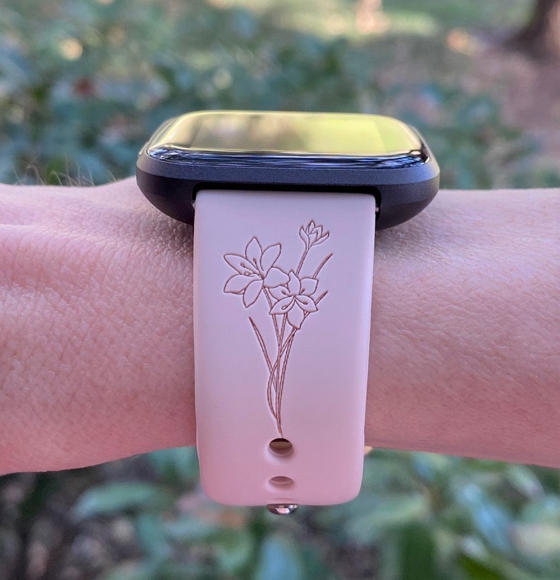 Op de afbeelding: Een zwarte smartwatch met een roze siliconen band met een bloemenpatroon. De band heeft een delicaat bloemenpatroon dat in het siliconen is ge&euml;tst.
