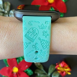 May include: A teal green smartwatch band with a Christmas-themed design. The band features a snowman, gingerbread man, candy canes, and Christmas trees.
