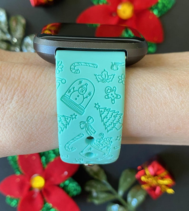 May include: A teal green smartwatch band with a Christmas-themed design. The band features a snowman, gingerbread man, candy canes, and Christmas trees.