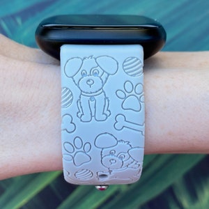 Puede incluir: Una correa de reloj de silicona gris con un patr&oacute;n en relieve blanco de perros, huesos y huellas de patas. La correa est&aacute; dise&ntilde;ada para un reloj inteligente.