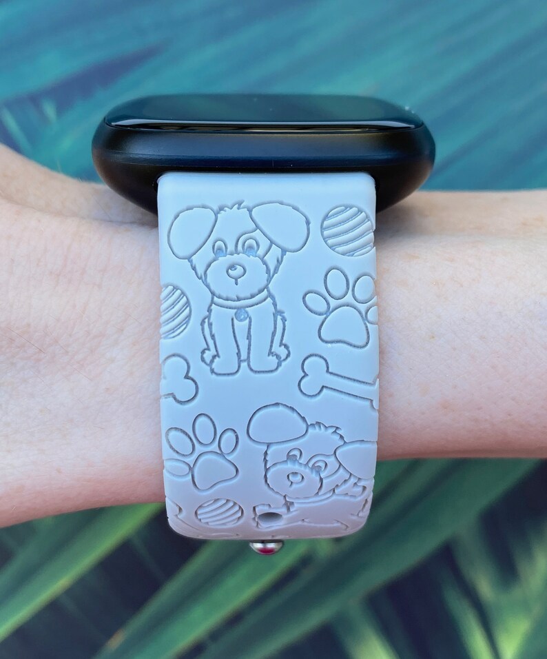 Puede incluir: Una correa de reloj de silicona gris con un patr&oacute;n en relieve blanco de perros, huesos y huellas de patas. La correa est&aacute; dise&ntilde;ada para un reloj inteligente.