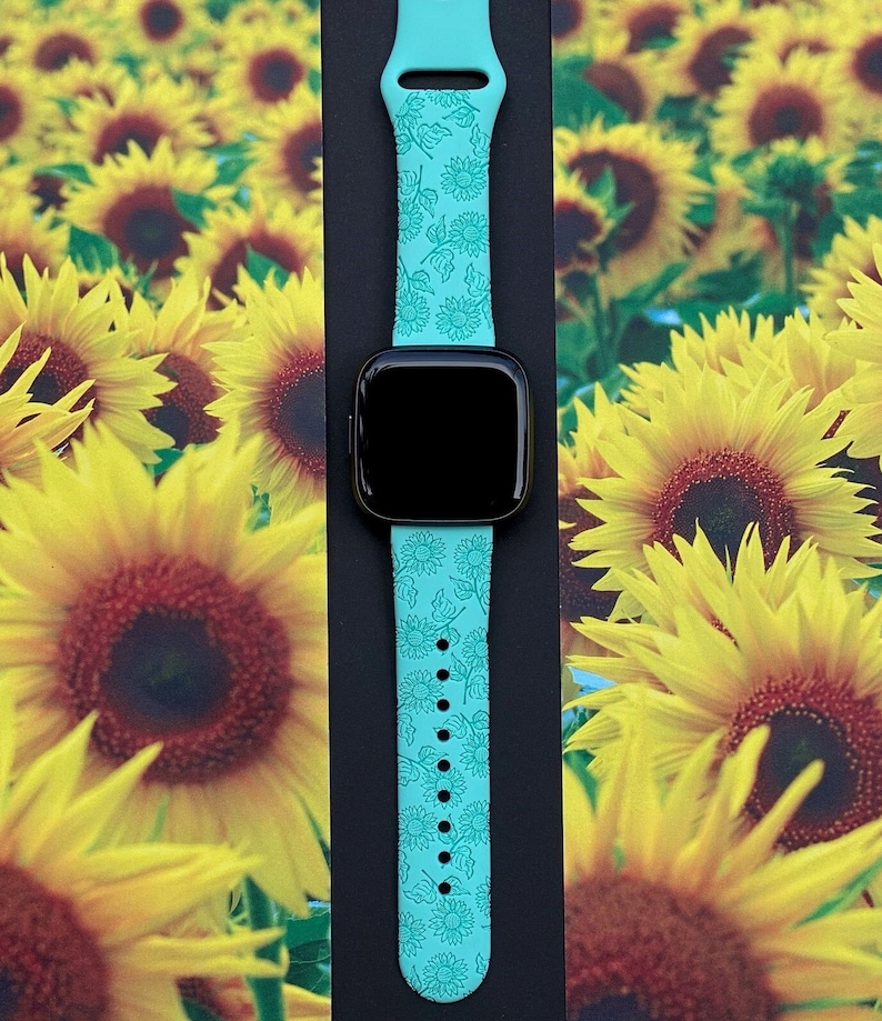 May include: A turquoise blue Apple Watch band with a sunflower pattern. The band is made of silicone and has a smooth finish.
