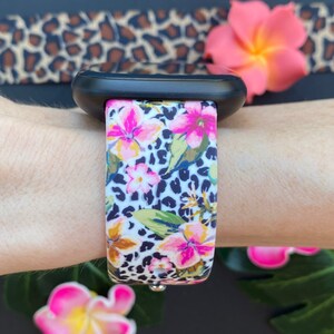 May include: A white and black leopard print watch strap with pink flowers. The strap is made of silicone and is compatible with Apple Watches.