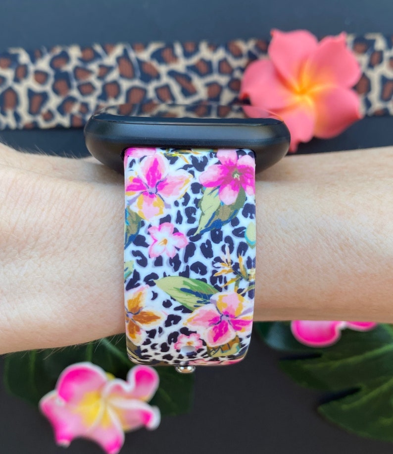 May include: A white and black leopard print watch strap with pink flowers. The strap is made of silicone and is compatible with Apple Watches.