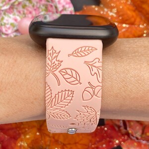 May include: A pink silicone watch band with a fall leaf design. The band has a black watch face and a silver buckle.