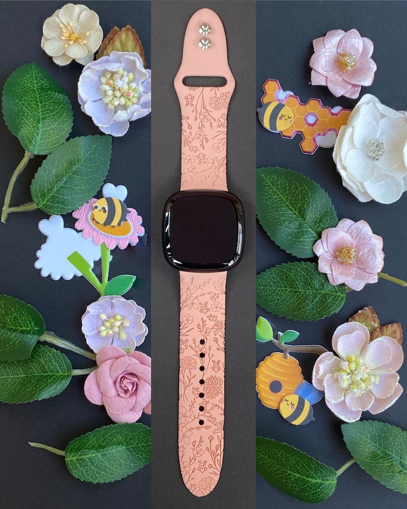 May include: A pink watch band with a floral and bee design. The band is made of silicone and has a black watch face.