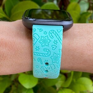 May include: A turquoise blue smartwatch band with a white snowflake, candy cane and heart pattern.