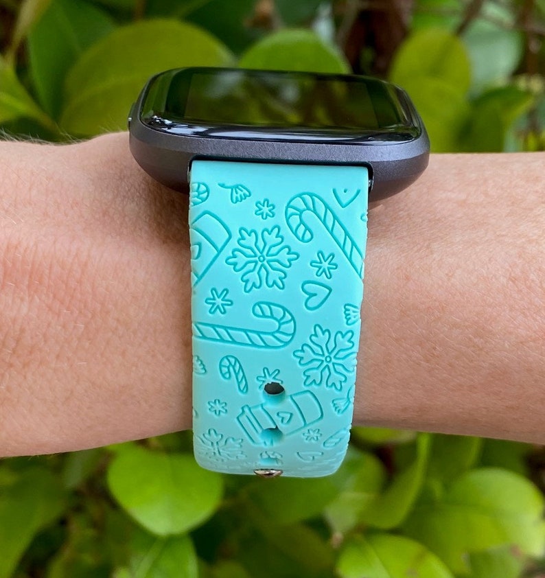 May include: A turquoise blue smartwatch band with a white snowflake, candy cane and heart pattern.