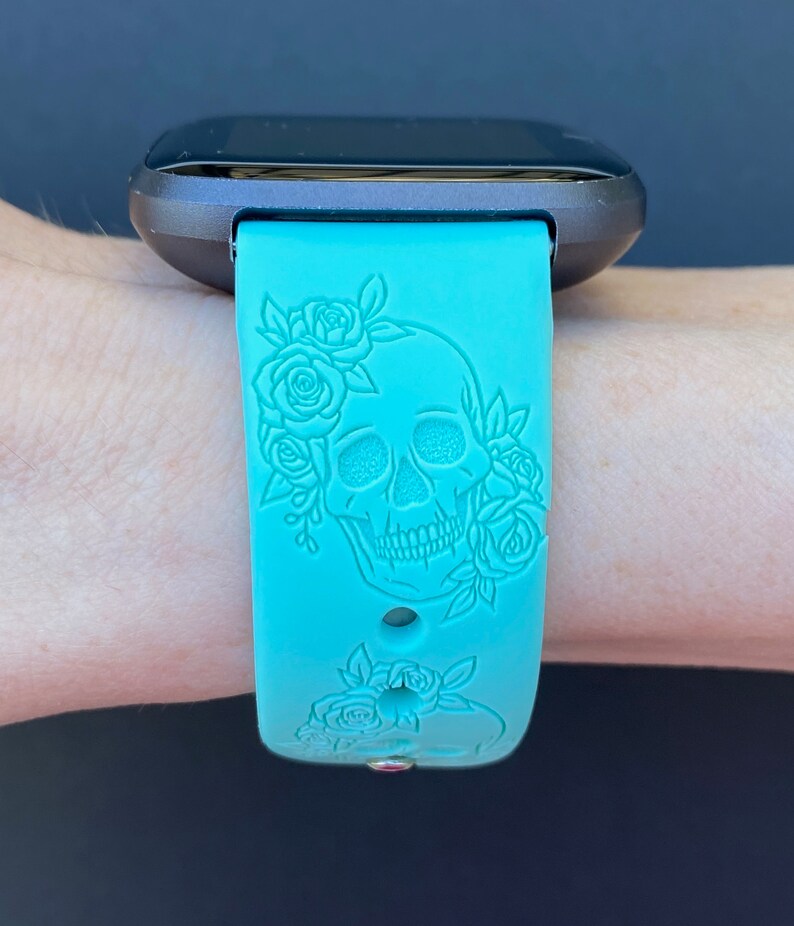 Op de afbeelding: Een turquoise blauwe siliconen horlogeband met een schedel- en rozenontwerp. De band is ontworpen voor een smartwatch.