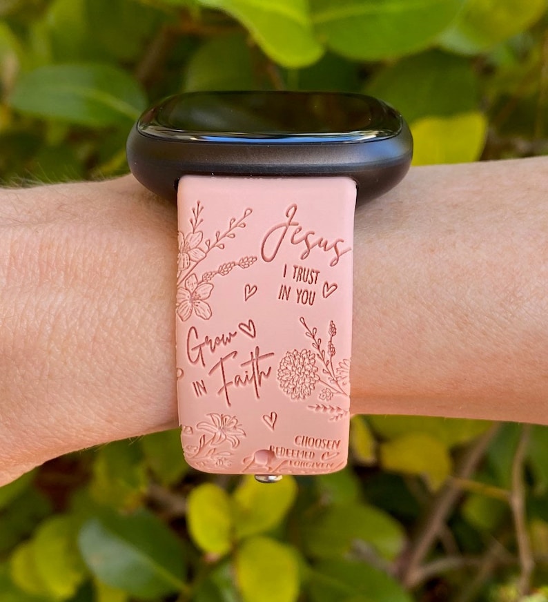May include: A pink silicone watch band with a floral design and the text "Jesus I trust in you" and "Grow in Faith". The band also has the text "Chosen Redeemed Forever".
