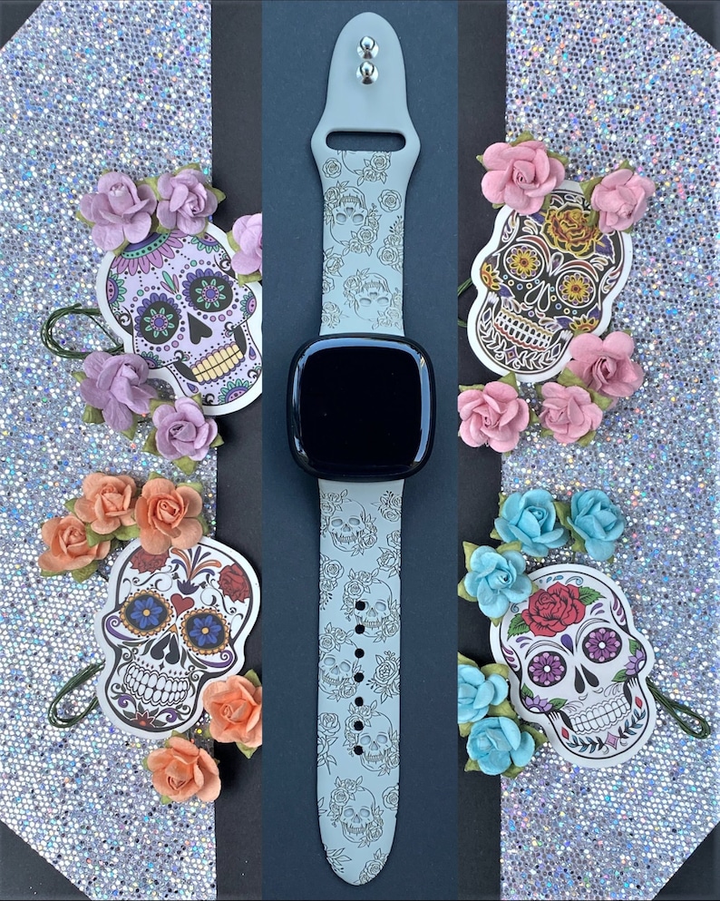 May include: A grey silicone watch band with a white and grey skull and flower pattern. The band is shown with four decorative sugar skull stickers.
