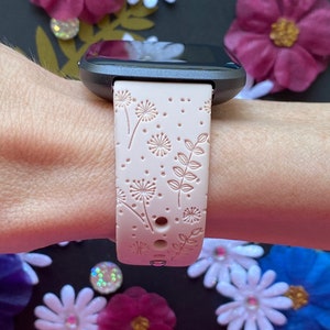 May include: A pink silicone watch band with a white floral pattern. The band is designed for a smartwatch with a square face.