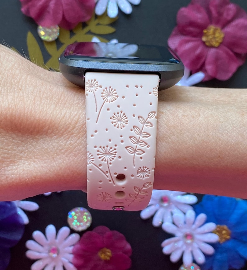 May include: A pink silicone watch band with a white floral pattern. The band is designed for a smartwatch with a square face.