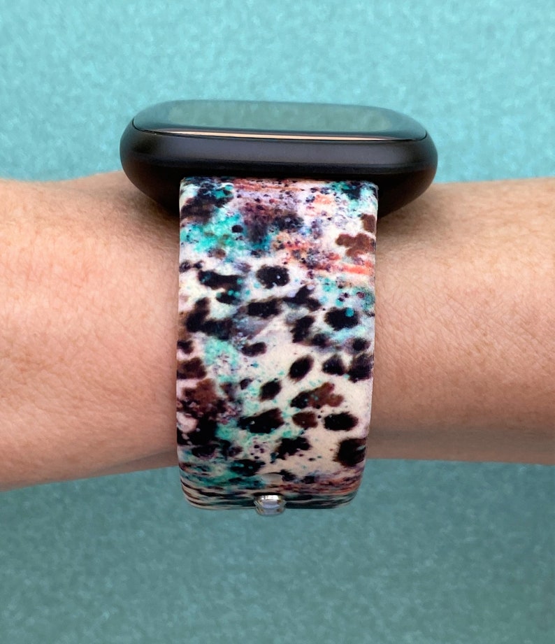 Puede incluir: Un reloj inteligente negro con una banda estampada en blanco, marr&oacute;n y azul. La banda tiene un dise&ntilde;o de estampado de leopardo.