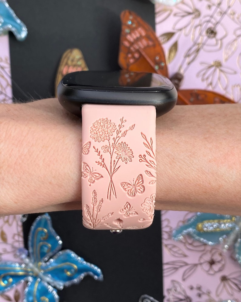 May include: A pink silicone watch band with a floral and butterfly design. The band is embossed with delicate flowers and butterflies.