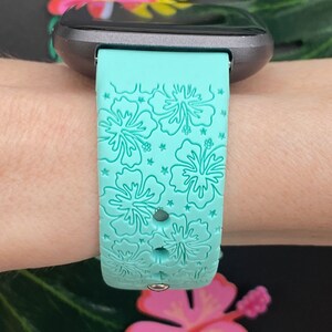 May include: A turquoise silicone watch band with a floral pattern. The band has a white hibiscus flower design.